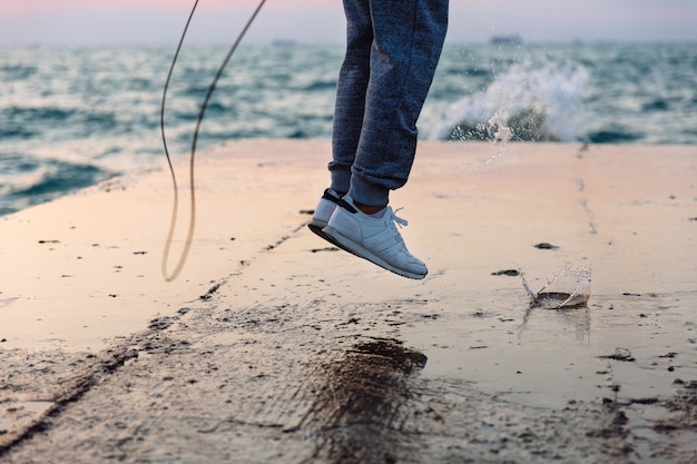 Nahaufnahmefoto des springenden Mannes in der Sportkleidung mit Springseil, Praxis auf Pier