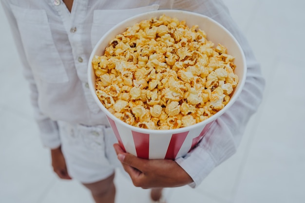 Nahaufnahmefoto eines jungen süßen Mädchens, das eine Tube Popcorn in ihren Händen hält.