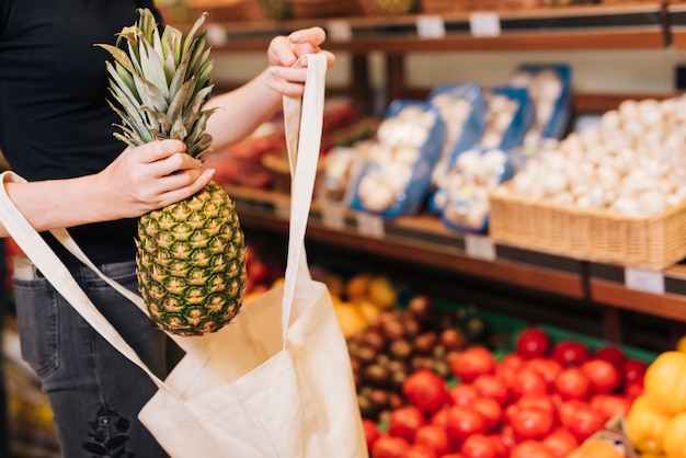 Nahaufnahmefrau, die eine Ananas in eine Tasche einsetzt