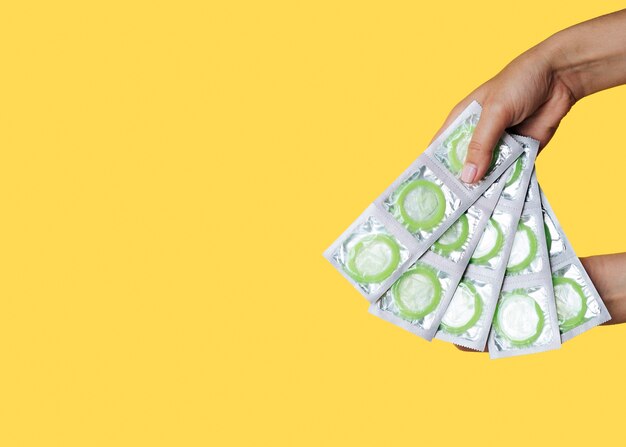 Nahaufnahmefrau, die eingewickelte grüne Kondome hält