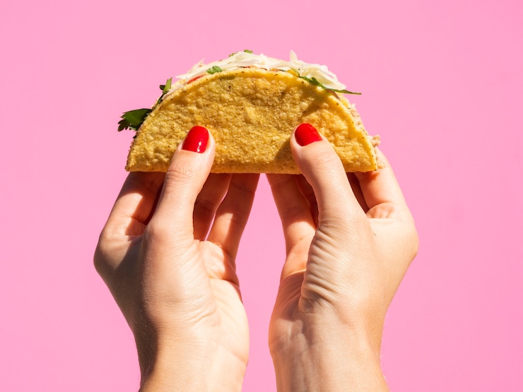 Kostenlose Foto nahaufnahmefrau, die taco mit rosa hintergrund hält