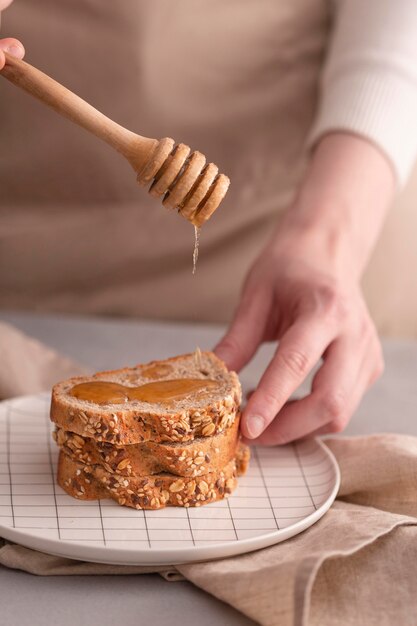 Nahaufnahmehände, die Honig auf Brot gießen