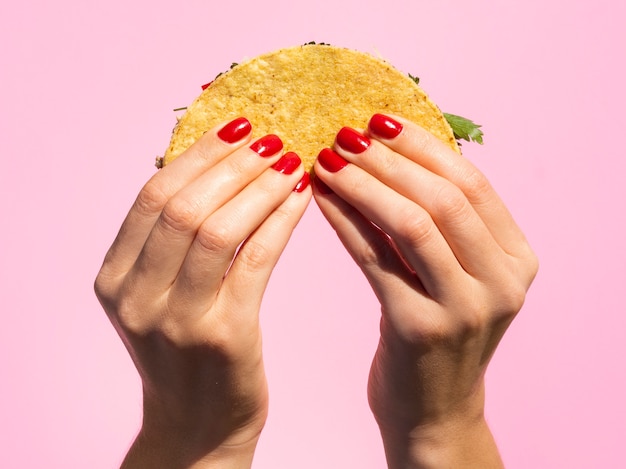 Kostenloses Foto nahaufnahmehände, die taco mit rosa hintergrund halten