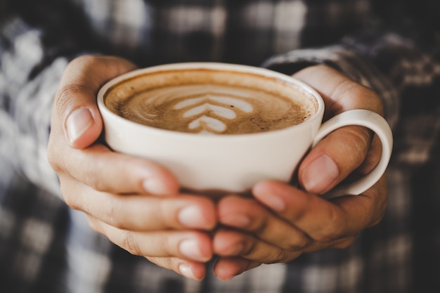 Nahaufnahmehand der Frau eine Kaffeetasse im Café halten, addieren den Retro- Farbton des Filters