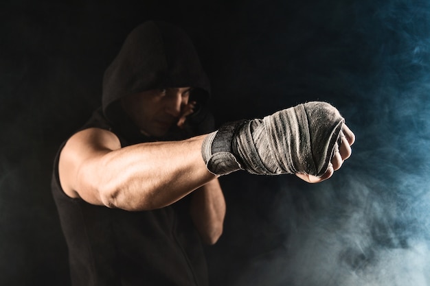 Kostenloses Foto nahaufnahmehand mit verband des muskulösen mannes, der kickboxen auf schwarzem und blauem rauch trainiert