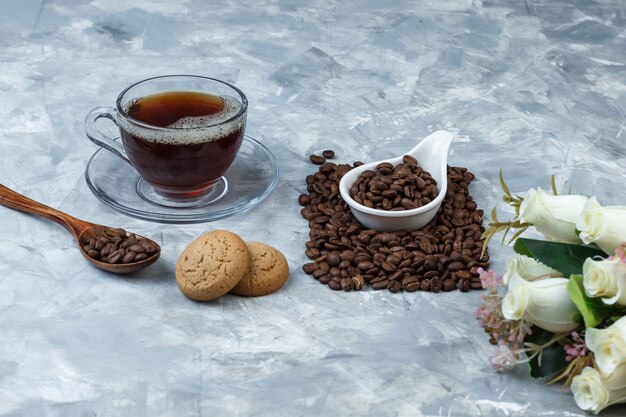 Nahaufnahmekaffeebohnen im weißen Porzellankrug mit Keksen, Tasse Kaffee, Blumen