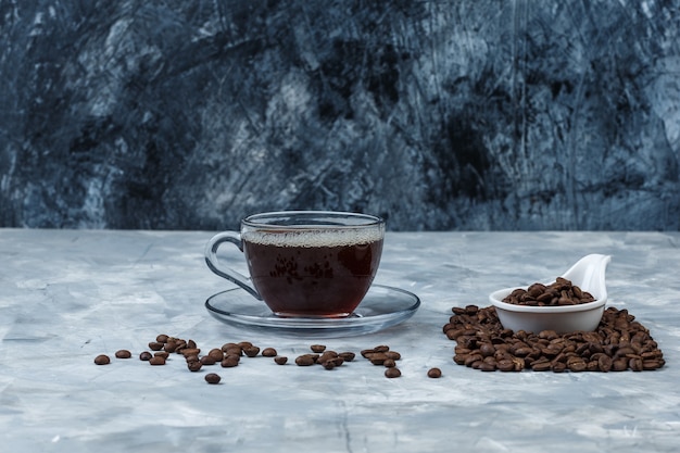 Nahaufnahmekaffeebohnen im weißen Porzellankrug mit Tasse Kaffee auf dunkelblauem und hellblauem Marmorhintergrund. horizontal