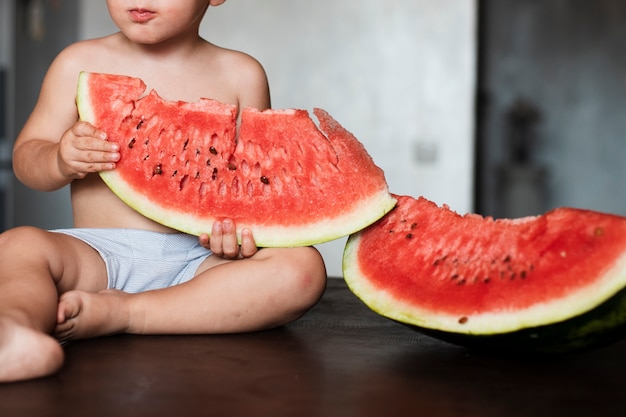 Kostenloses Foto nahaufnahmekind, das scheibe der wassermelone hält