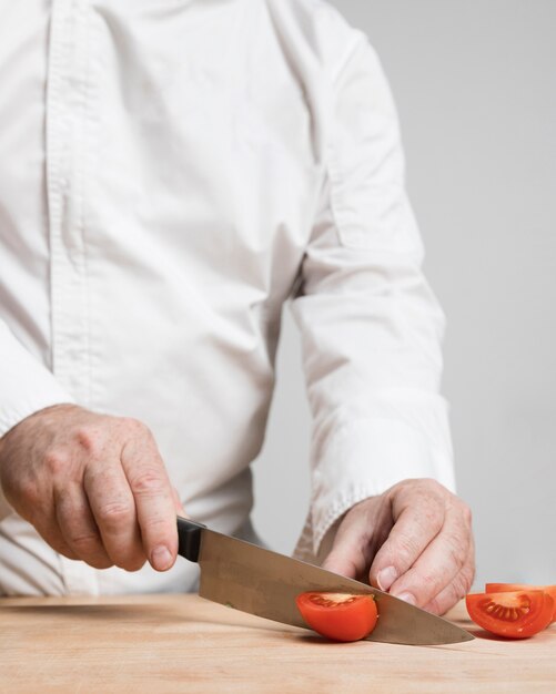 Nahaufnahmekoch, der Tomaten auf Holzbrett schneidet