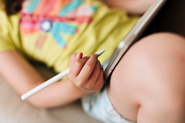 Nahaufnahmemädchen, das auf der Couch mit Tablette und Stift sitzt