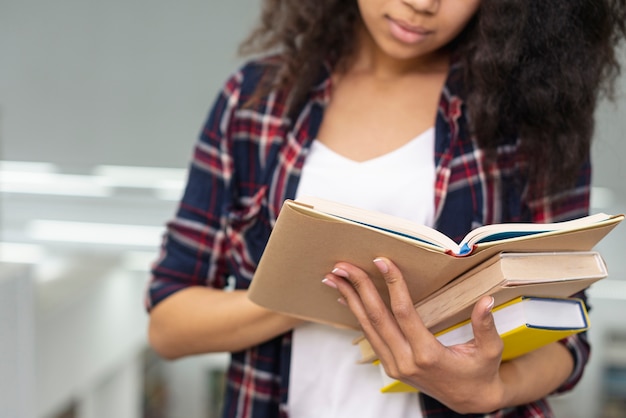 Nahaufnahmemädchen, das Stapel Bücher beim Lesen trägt