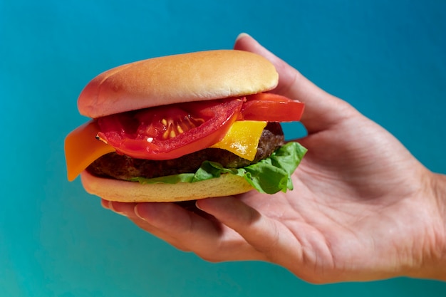 Kostenloses Foto nahaufnahmeperson, die geschmackvollen cheeseburger mit blauem hintergrund hält