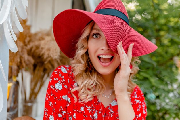 Nahaufnahmeporträt der attraktiven stilvollen blonden lächelnden Frau im strohroten Hut und im Blusensommermode-Outfit mit Lächeln