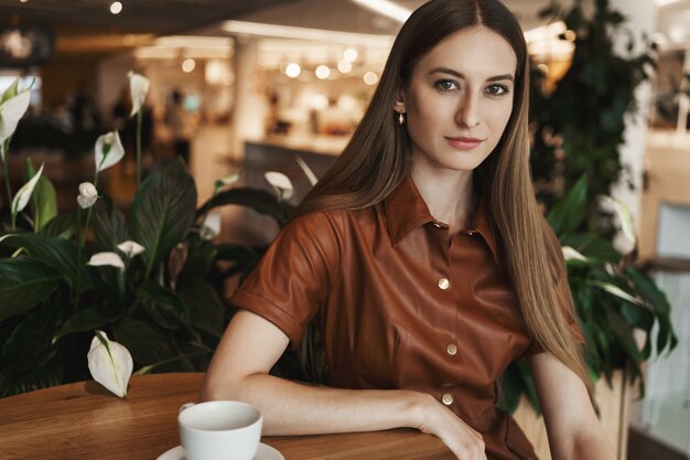 Nahaufnahmeporträt der eleganten charmanten jungen Frau, die sich auf einen Kaffeetisch in einem Café stützt.