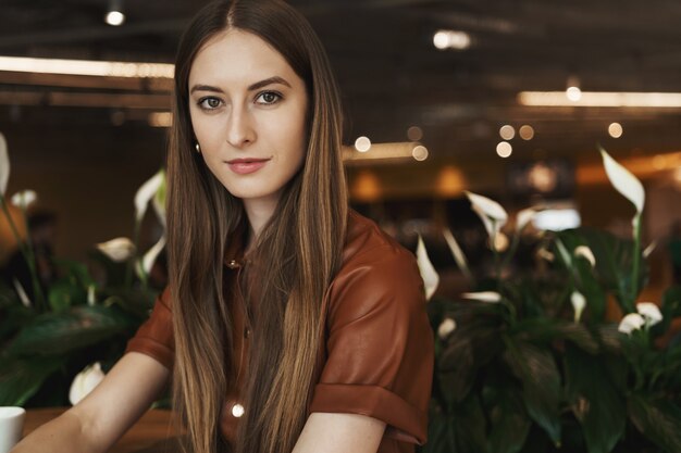 Nahaufnahmeporträt der eleganten charmanten jungen Frau, die sich auf einen Kaffeetisch in einem Café stützt.