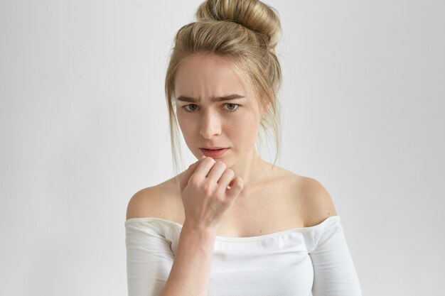 Nahaufnahmeporträt der enttäuschten ernsten jungen Frau mit den Sommersprossen, die Stirn runzeln, angespannten fokussierten Blick haben, ihre Lippen berühren, während sie über ein Problem nachdenken. Menschliche Emotionen, Gefühle und Reaktionen