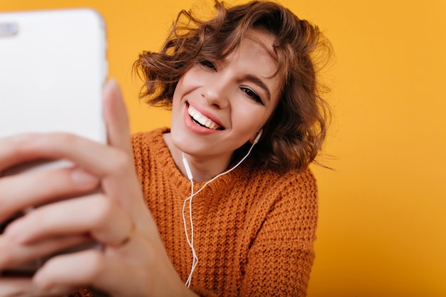 Nahaufnahmeporträt der erfreuten weißen Frau mit lässigem Make-up, das Foto mit ihrem Telefon macht