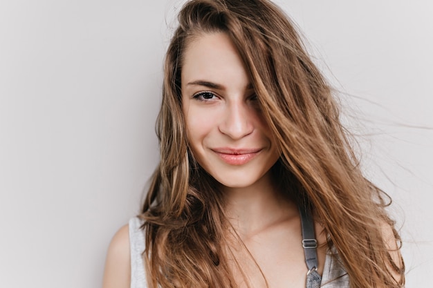 Nahaufnahmeporträt der europäischen Frau mit den großen dunklen Augen lokalisiert. Foto des charmanten Mädchens mit hellbraunem Haar, das mit Lächeln aufwirft.