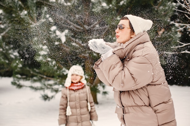 Nahaufnahmeporträt der Frau in der braunen Jacke im verschneiten Park mit ihrer Tochter
