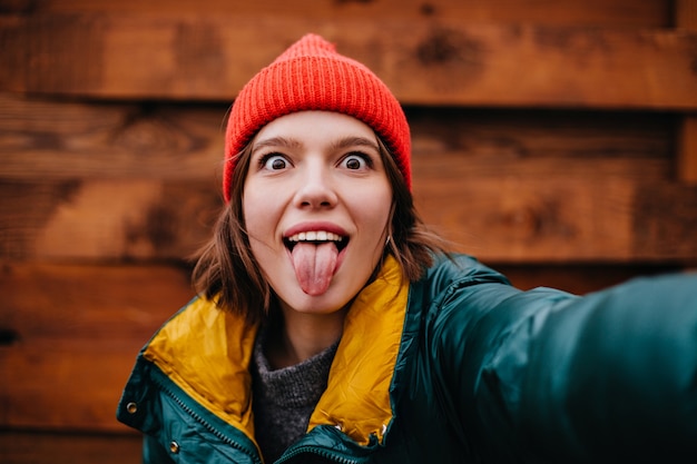 Nahaufnahmeporträt der frechen Teenagerfrau, die selfie auf Holzwand nimmt