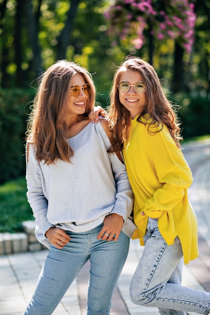 Kostenloses Foto nahaufnahmeporträt der freundlichen glücklichen mädchen mit dem aufstellen in hellen gläsern außerhalb. zwei junge damen mit schönem gesichtsausdruck verbringen zeit miteinander