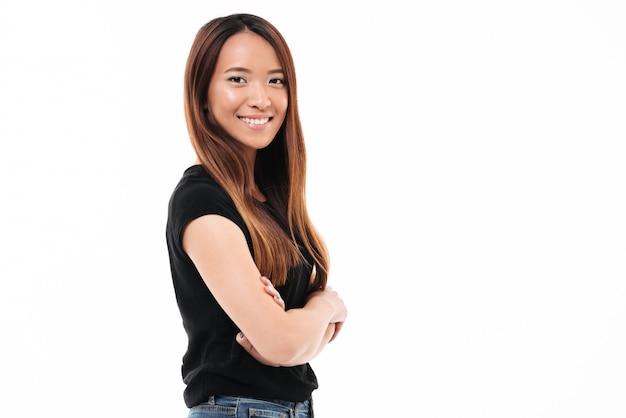 Nahaufnahmeporträt der fröhlichen jungen asiatischen Frau, die mit gekreuzten Händen steht und Kamera betrachtet