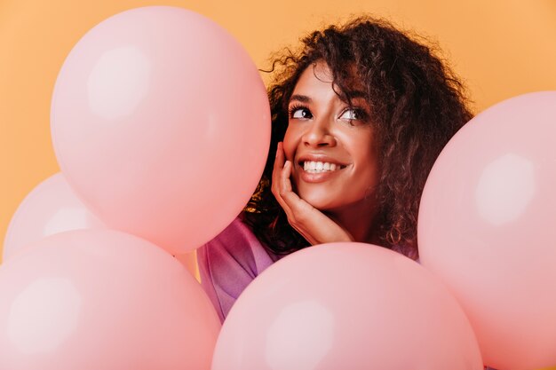 Nahaufnahmeporträt der gewinnenden schwarzen Frau, die Spaß an der Geburtstagsfeier hat. Schönes afrikanisches Mädchen, das mit rosa Luftballons aufwirft.