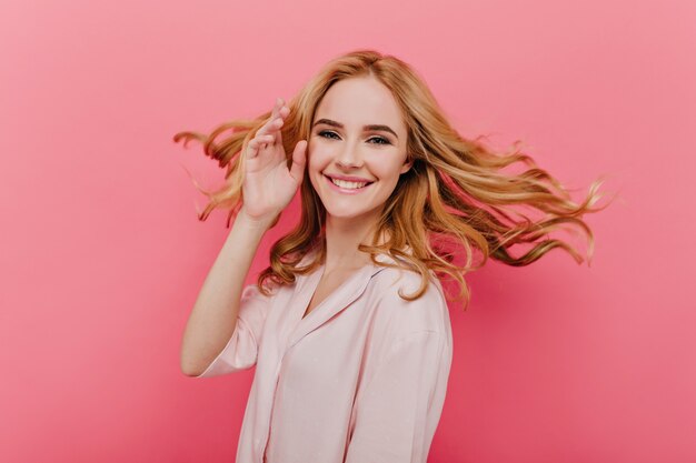 Nahaufnahmeporträt der glücklichen jungen Frau mit den schönen blonden Haaren lokalisiert auf rosa Wand. Foto der fröhlichen kaukasischen Dame trägt Baumwollnachtanzug.