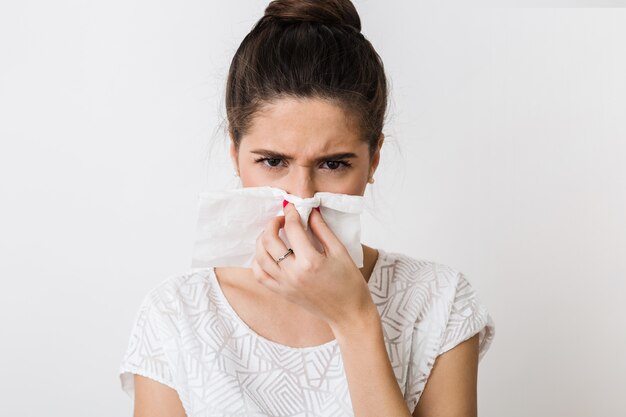 Nahaufnahmeporträt der hübschen Frau, die ihre Nase mit Serviette putzt, sich erkältet, sich krank, isoliert, stirnrunzelnd fühlt