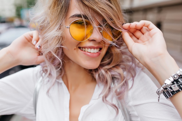 Nahaufnahmeporträt der inspirierten jungen Frau, die ihr blondes Haar lacht und berührt