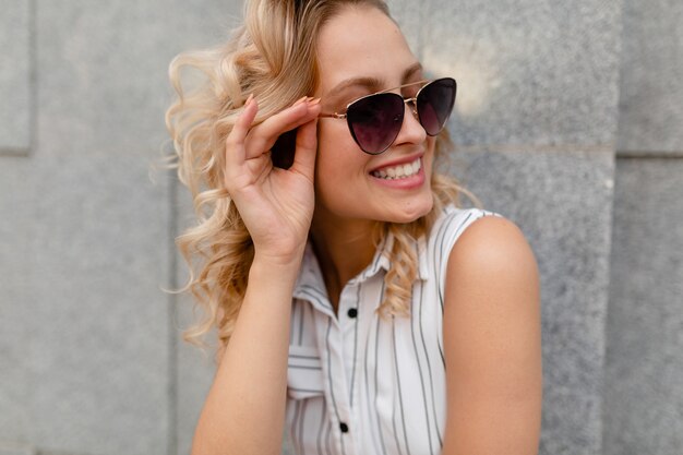 Nahaufnahmeporträt der jungen attraktiven stilvollen blonden Frau in der Stadtstraße im Sommermodeartkleid, das Sonnenbrille trägt