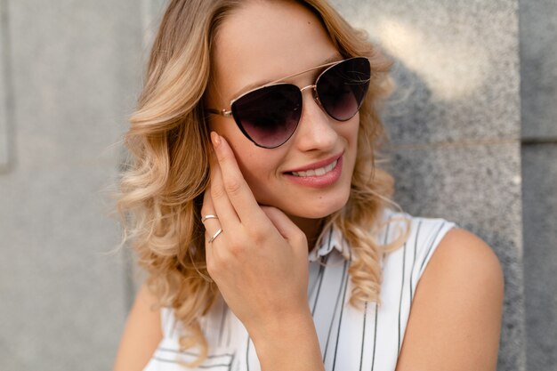 Nahaufnahmeporträt der jungen attraktiven stilvollen blonden Frau in der Stadtstraße im Sommermodeartkleid, das Sonnenbrille trägt