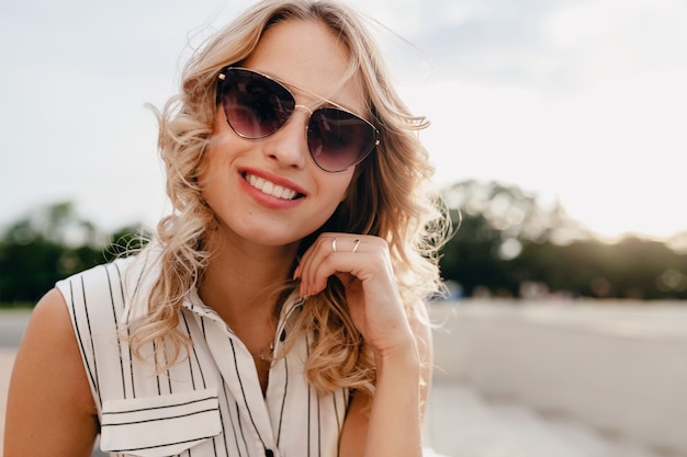 Nahaufnahmeporträt der jungen attraktiven stilvollen blonden Frau in der Stadtstraße im Sommermodeartkleid, das Sonnenbrille trägt