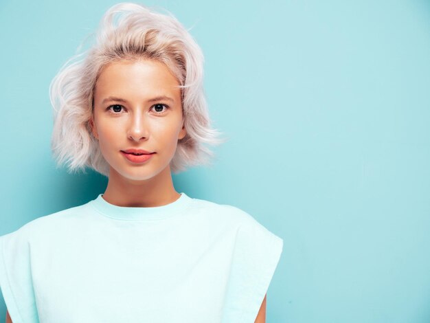 Nahaufnahmeporträt der jungen schönen lächelnden Frau in der modischen Sommerkleidung Sexy sorglose Frau, die nahe blauer Wand im Studio aufwirft Positives blondes Modell, das Spaß hat und verrückt geht Fröhlich und glücklich