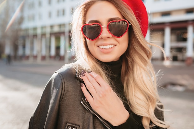 Kostenloses Foto nahaufnahmeporträt der modischen blonden frau im roten hut und in der stilvollen sonnenbrille, die in der straße gehen. mode frühling sommer foto der entzückenden frau