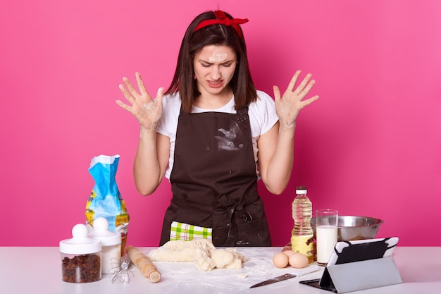 Nahaufnahmeporträt der müden Hausfrau oder des Bäckers sieht traurig aus, verbringt viele Stunden damit, Osterkuchen zuzubereiten, kann nicht die gewünschte Konsistenz des Teigs herstellen, will aufhören zu backen, isoliert auf Rosa.