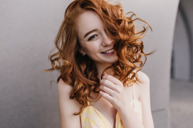 Nahaufnahmeporträt der positiven glamourösen Frau mit den roten Haaren. Lächelndes kaukasisches Mädchen, das Glück auf grauer Wand ausdrückt.