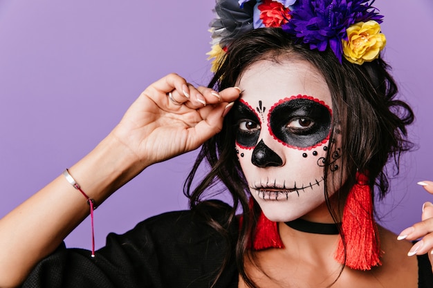 Nahaufnahmeporträt der raffinierten Frau mit den dunklen Augen, die im Maskeradekostüm aufwerfen. Nette lateinische Dame im Blumenkranz, der für Halloween vorbereitet.