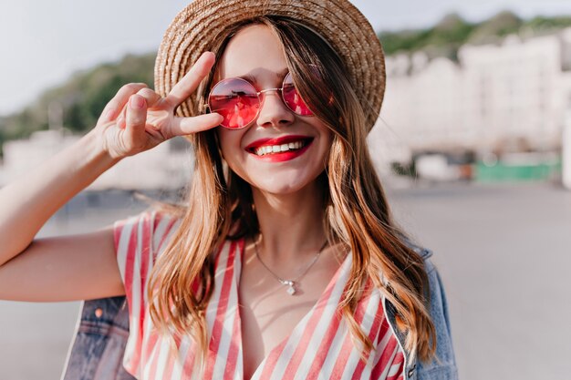 Nahaufnahmeporträt der scherzhaften blonden Frau in der stilvollen rosa Sonnenbrille. Prächtiges kaukasisches Mädchen, das positive Emotionen am Sommertag ausdrückt.