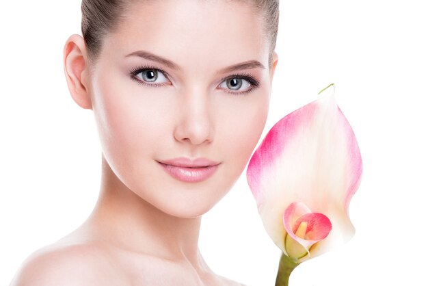 Nahaufnahmeporträt der schönen jungen hübschen Frau mit gesunder Haut und rosa Blumen nahe Gesicht - lokalisiert auf Weiß.
