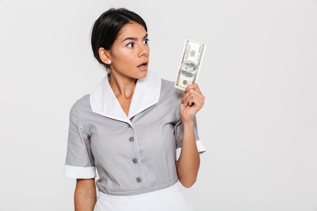 Nahaufnahmeporträt der überraschten jungen Frau in der Uniform, die Hundert-Dollar-Banknote hält