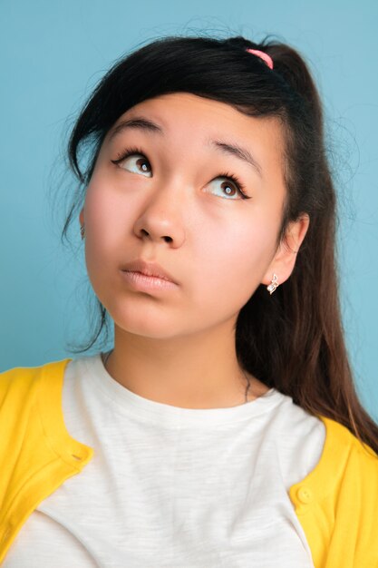 Nahaufnahmeporträt des asiatischen Teenagers lokalisiert auf blauem Raum. Schönes weibliches brünettes Modell mit langen Haaren