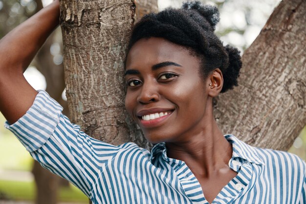 Nahaufnahmeporträt des attraktiven afroamerikanischen jugendlich Mädchens, das am Baum aufwirft