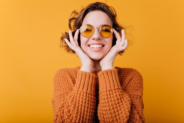 Nahaufnahmeporträt des blassen kaukasischen Mädchens mit dem schönen Lächeln. Foto der entspannten europäischen Frau trägt runde gelbe Sonnenbrille.