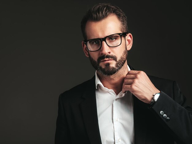 Nahaufnahmeporträt des gutaussehenden, selbstbewussten, stilvollen Hipster-Lambersexual-Modells Sexy moderner Mann, gekleidet in eleganten schwarzen Anzug Modemann, der im Studio auf dunklem Hintergrund in Brillen posiert