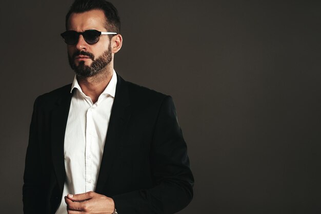 Nahaufnahmeporträt des gutaussehenden, selbstbewussten, stilvollen Hipster-Lambersexual-Modells Sexy moderner Mann, gekleidet in eleganten schwarzen Anzug Modemann posiert im Studio auf dunklem Hintergrund mit Sonnenbrille