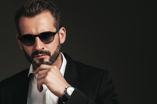 Nahaufnahmeporträt des gutaussehenden, selbstbewussten, stilvollen Hipster-Lambersexual-Modells Sexy moderner Mann, gekleidet in eleganten schwarzen Anzug Modemann posiert im Studio auf dunklem Hintergrund mit Sonnenbrille
