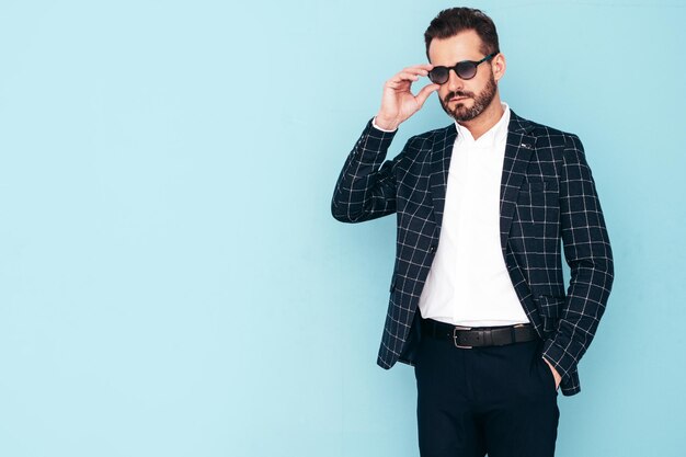 Nahaufnahmeporträt des gutaussehenden, selbstbewussten, stilvollen Hipster-Lambersexual-Modells Sexy moderner Mann in schwarzem, elegantem Anzug Modemann, der in der blauen Wand des Studios posiert