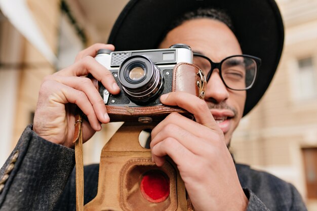 Nahaufnahmeporträt des hübschen schwarzen Mannes in den eleganten Gläsern, die Fotos mit Kamera machen. Konzentrierter afrikanischer Fotograf, der im Freien arbeitet.