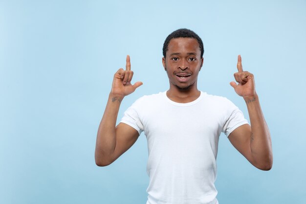 Nahaufnahmeporträt des jungen afroamerikanischen Mannes im weißen Hemd. Leere Leiste zeigend, zeigend, wählend, einladend.